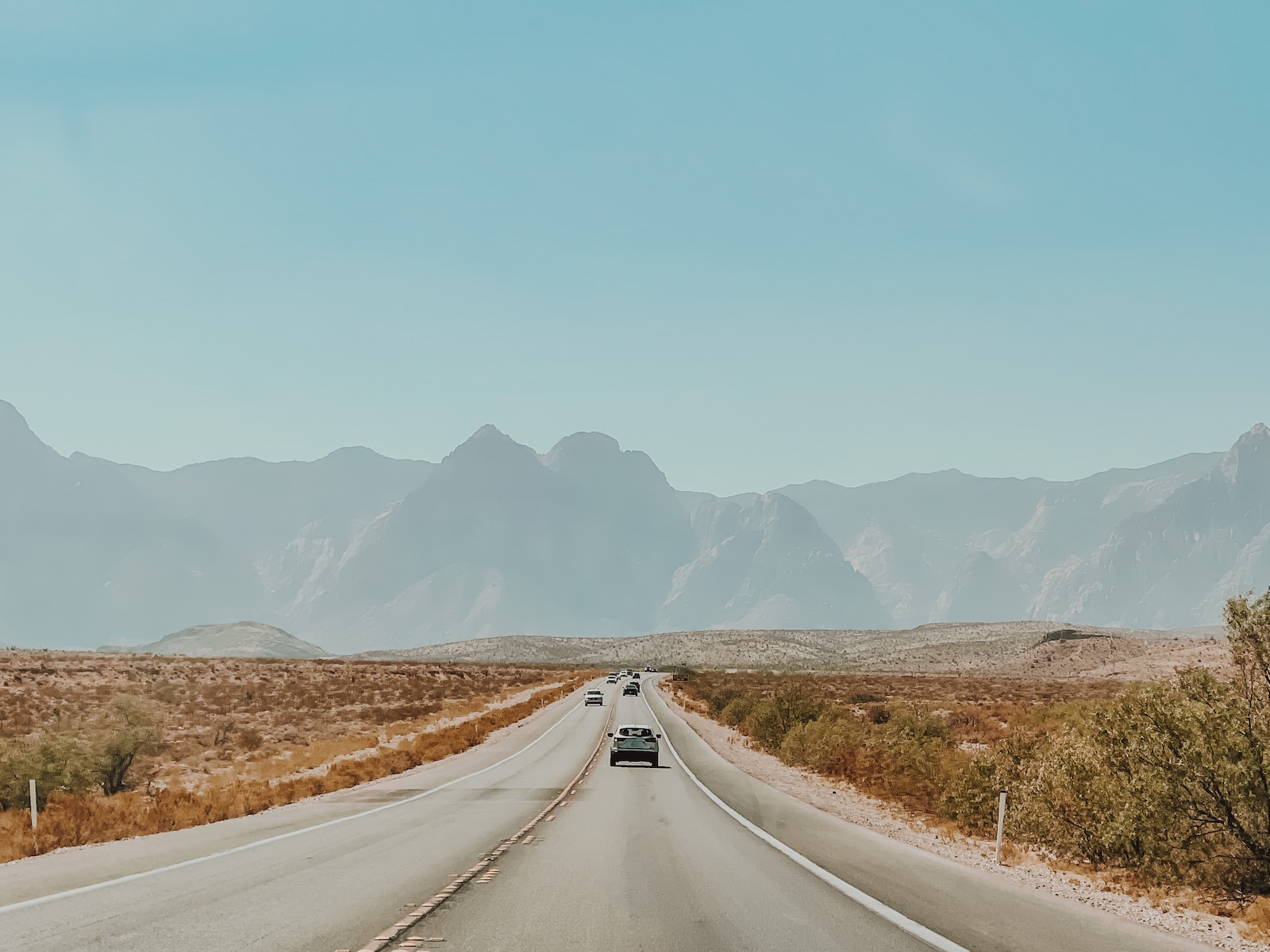 a car driving down a desert road with mountains in the background
